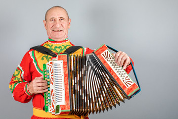 Portrait of a man in a national costume, grandfather plays the accordion. On a gray background.