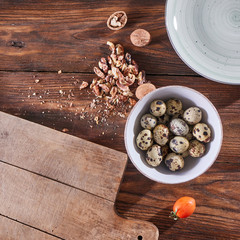 Obraz na płótnie Canvas A bowl with quail eggs, pieces of walnut and a wooden board on the kitchen table with copy space. Ingredients for Healthy Salad. Flat lay