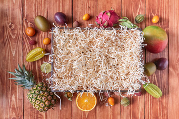 Set of different exotic fruits around an empty wooden box on a brown wooden background with copy...
