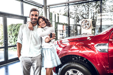 Happy young lovely couple in casual wear hugging while buying first new family car together in...