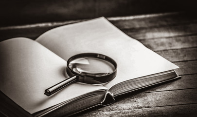 magnifying glass and book on wooden table. Image in black and white color style