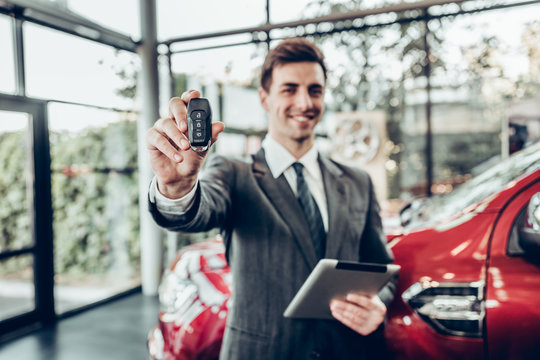 Salesman in grey suit holding car key on red car background
