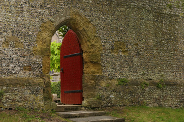 Rote ge&ouml;ffnete T&uuml;r in Mauerwand zu verstecktem Garten
