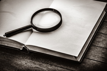 magnifying glass and book on wooden table. Image in black and white color style