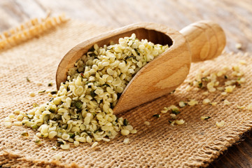 Heap of raw, organic hemp seeds in wooden scoop on burlap on rustic table