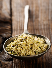 Heap of raw, organic hemp seeds in metal scoop on brown rustic wooden table