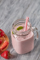 Milk smoothie with strawberries, mint leaves and chia seeds in a glass jar with a straw on a wooden table with copy space. Healthy drink