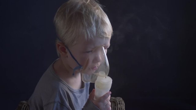 Caucasian blonde boy inhales couples containing medication from inhaler to stop coughing. Medical procedures. Inhaler. Respiratory medicine. Bronchitis, asthmatic health problem. Home treatment breath