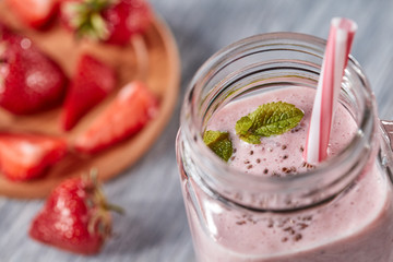 Closeup of organic milky strawberry smoothie with chia seeds and mint leaves in a glass with a straw on a wooden table. Healthy dessert. Top view