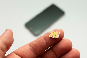 nano sim card on the finger on the background of the smartphone lying in the defocus, on a white background