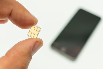 nano sim card in hand on the background of the smartphone lying in the defocus, on a white background