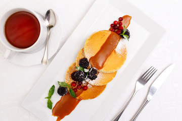 Pancakes with berries and maple syrup isolated in white.