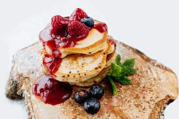 Pancakes with berries and maple syrup isolated in white