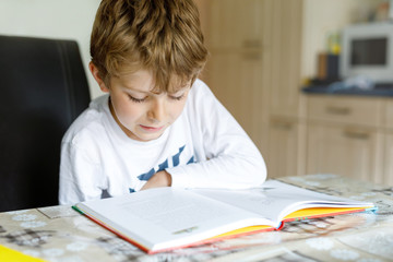 Little blonde school kid boy reading a book at home. Child interested in reading magazine for kids. Leisure for kids, building skills and education concept