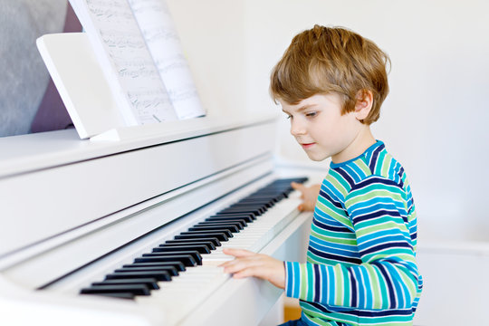 Beautiful little kid boy with headphones playing piano in living room or music school. Preschool child having fun with learning to play music instrument. Education, skills concept
