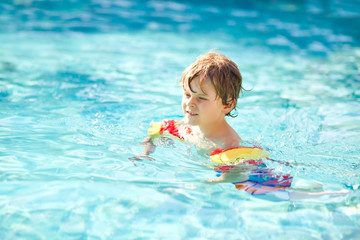 Fototapeta na wymiar Happy little kid boy having fun in an swimming pool. Active happy healthy preschool child learning to swim. with safe floaties or swimmies. Family, vacations, summer concept