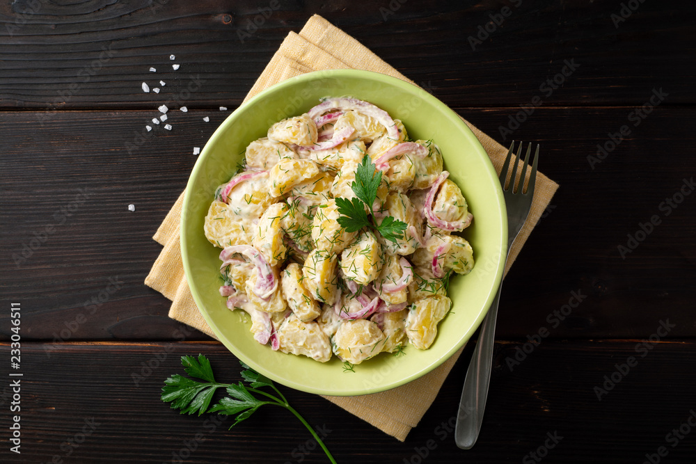 Wall mural Potato salad with red onion and greens in bowl on dark wooden table. Top view. Copy space.