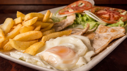 Fried egg with loin, french fries and tomato salad