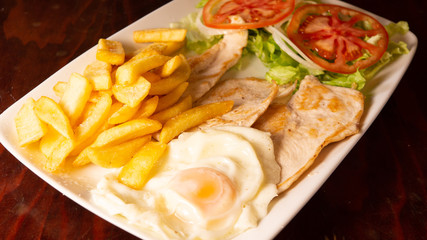 Fried egg with loin, french fries and tomato salad