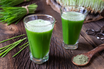 Two glasses of barley grass juice with fresh barley grass blades in the background