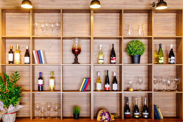 Bottles of white and red wine on a wooden shelf with books in private winery cabinet room interior - obrazy, fototapety, plakaty