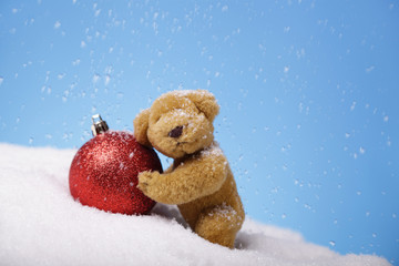 Vintage teddy bear pushing  a red Christmas bauble outdoors on a snowy day