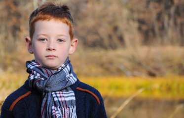 child in a checkered scarf on the background of the autumn river, blurred background, close-up.