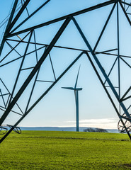 Fototapeta premium Wind Turbine seen through frame of an electricity pylon with blue sky