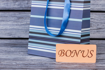 Blue shopping bag on wooden background. Gift bag and card with written inscription bonus. Marketing and sales. Concept of bonus pay.