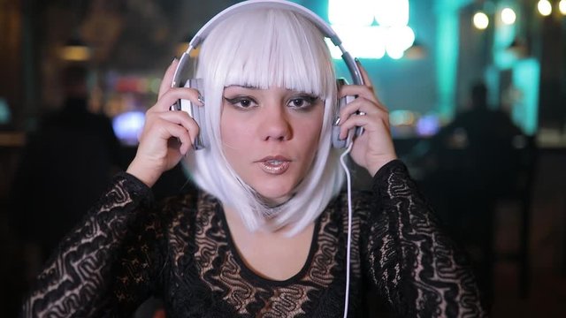 Unusual blonde girl listening to music in a bar using headphones