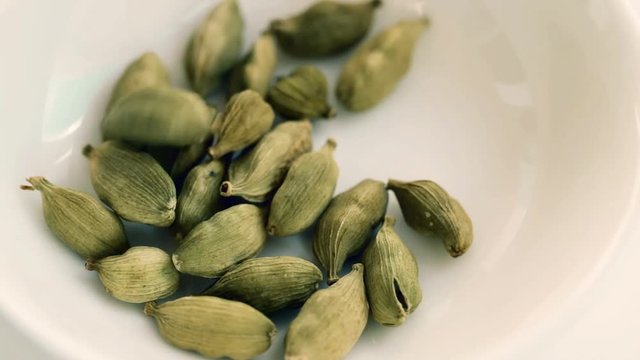 Pouring dry green cardamom seeds - famous aromatic spice into white bowl. Closeup. Selective focus. Macro shot of cardamon seeds.