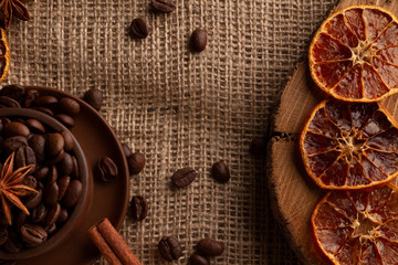High contrast photo of dried oranges, Arabica and Robusta seeds in a stein on a saucer with cinnamon and anise. View from above. Photo on a gray textured canvas burlap.