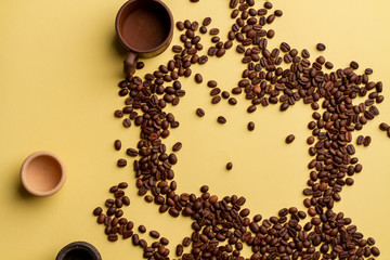 Chaotic scattered coffee beans arabica and robusta on a yellow paper background. Randomly placed clay cups between coffee beans. Photos with a clear focus.