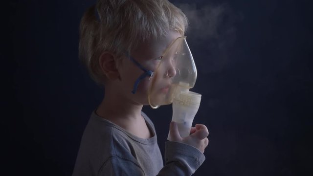 Caucasian blonde boy inhales couples containing medication from inhaler to stop coughing. Medical procedures. Inhaler. Respiratory medicine. Bronchitis, asthmatic health problem. Home treatment breath