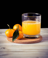 a glass of tangerine juice on a wooden table, three mandarins, dark background