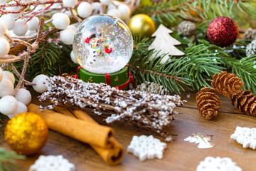 Snow globe with snowman amid christmas decoration on brown wooden surface with snowflakes, fir,...