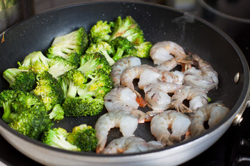 Preparation of shrimps with broccoli on frying pan