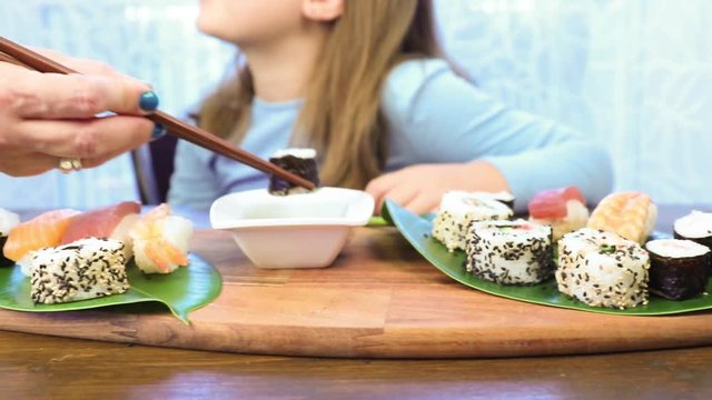 Mother is feeding her daughter with sushi 