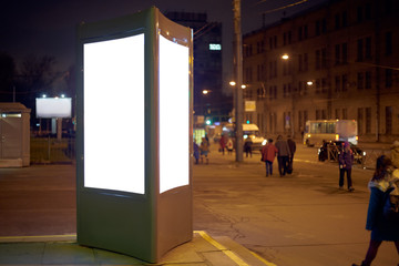 advertising pillar outdoor glowing on the background of the night city. mockup with a white field for advertising.