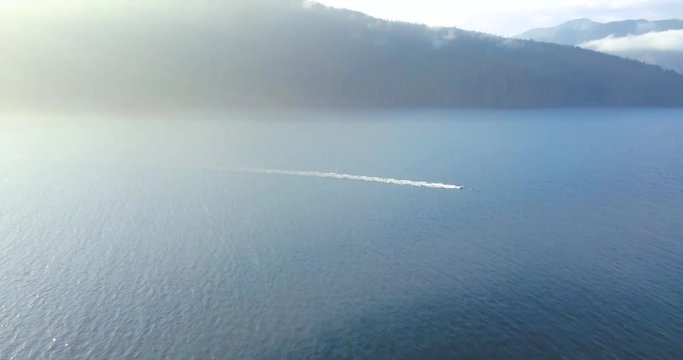 Lonely boat near the West Coast Trail, emerging from the sun lit fog. Aerial slowly panning upwards.