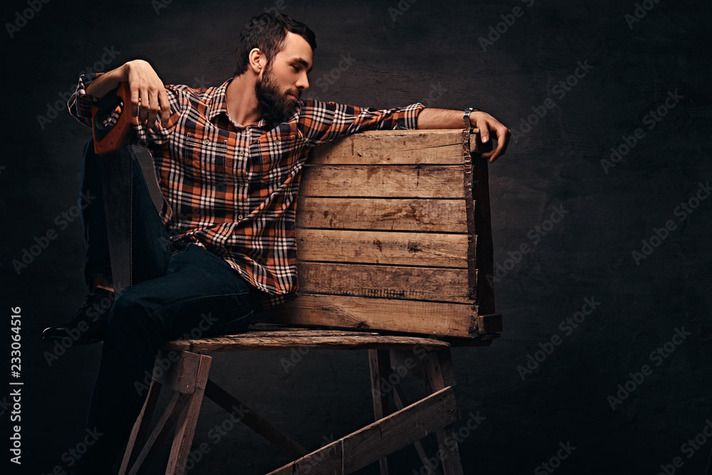 Wall mural Worker, carpenter, handyman holding a saw in a studio, isolated on a dark background.