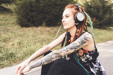 young girl with tattoo and dreadlocks listening to music in the park