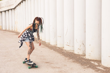 young girl with tattoo rides on a longboard