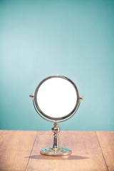 Retro silver makeup mirror frame on aged oak wooden table front mint blue wall background. Vintage style filtered photo
