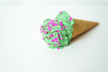 Ice cream cone. mint chocolate chip, peppermint bon bon ice cream with pink sprinkles in a waffle cone laying on side melting on white background. 