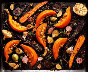 Baked vegetables with the addition of olive oil, aromatic herbs and spices on a dark background,...