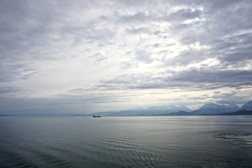 Fototapeta na wymiar Cook Inlet, Alaska, USA: A freighter on the horizon against mountains shrouded in morning mist, with dense, dramatic clouds overhead.