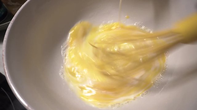 Close up shot of a woman mixing eggs with milk to make pancakes in a mixing bowl using a yellow whisk