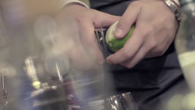 Close-up shot of bartender's hands cutting raw, ripe and fresh green lime on black cutting desk. Exotic fruity beverage preparation composition. Process of making Caipirinha cocktail on bar counter