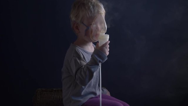 Caucasian blond child is crying from spasm of bronchitis and inhales vapors containing medications from inhaler to stop choking. Medical procedures. Respiratory medicine. Bronchitis, asthmatic problem